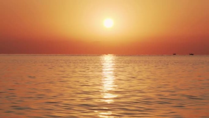 在太阳日出的背景下，用小浪缓慢地运动海面。一大片太阳升起在海面之上，这是水面上的太阳路径。海洋全景的