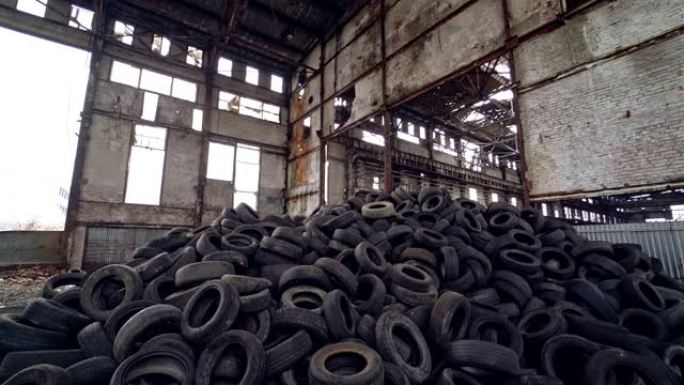 旧的灰色墙壁背景下，一堆旧的汽车轮胎在废弃的工厂内的地面上