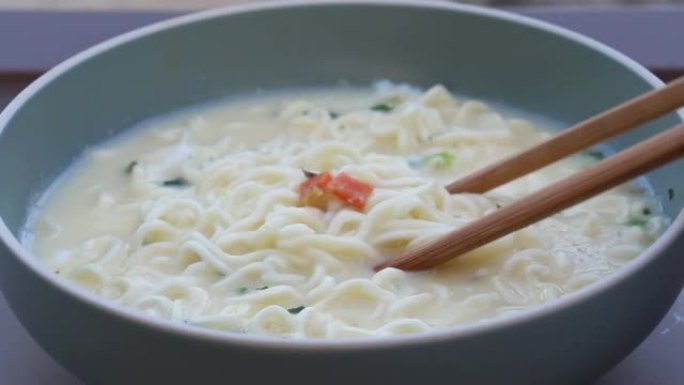女人用手拿筷子在碗里吃方便面，它的设计是在吃鸡蛋和蔬菜之前先煮熟或浸泡在沸水中，然后再加上热汤。