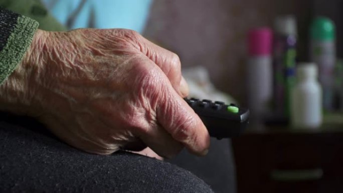 一位老人在看电视，娱乐，用遥控器关闭奶奶的满是皱纹的手。