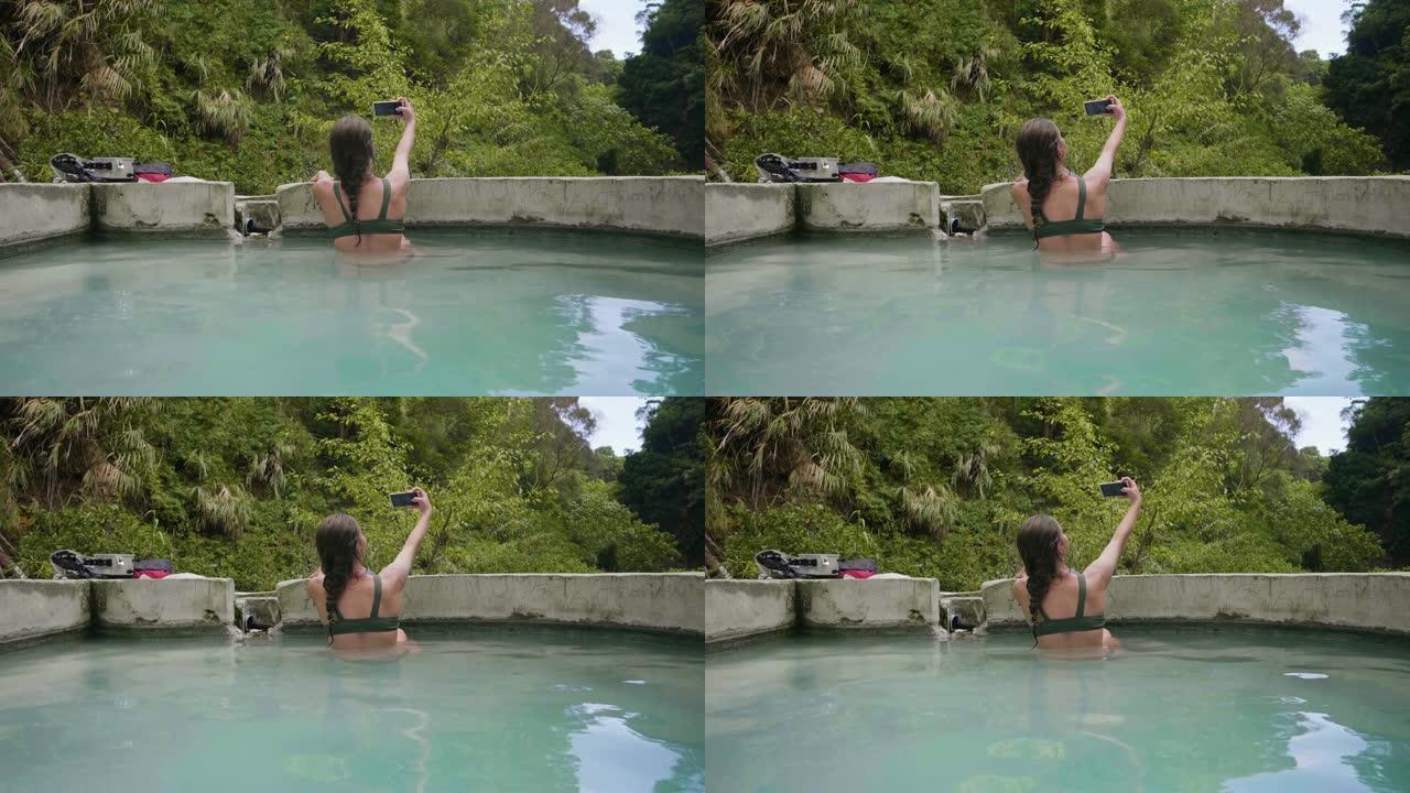 黑发女人在游泳池里洗热水澡，在自然水疗度假村摆姿势自拍。年轻女子在热带度假胜地的户外水疗中心自拍。