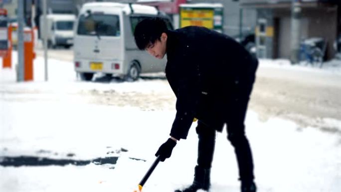 男子在冬天铲雪，而汽车在城市环境中行驶