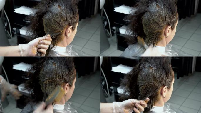 美发师-造型师将女人的头发分成几股，并用美发刷在头发上涂上油漆。染发程序。头发护理。后视图。4 k.