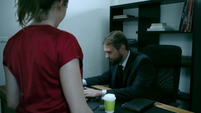 大胡子的商人坐在办公室的笔记本电脑上，穿红色衣服的女孩试图引诱老板，慢动作