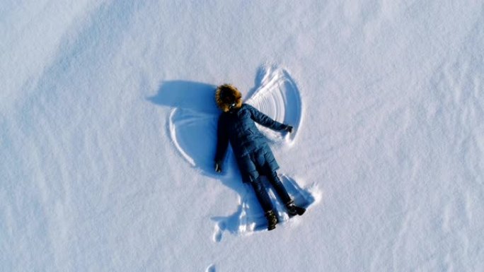 女人让雪天使躺在雪中。航拍视频。摄像机慢慢移开。
