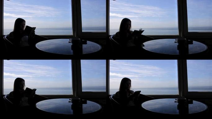年轻漂亮女孩的长镜头轮廓的长镜头坐在咖啡馆里，可以看到大西洋的全景。早上喝杯咖啡，茶，书，记事本，阅