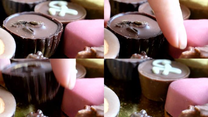 女人从盒装美味甜点背景中选择什锦巧克力。特写