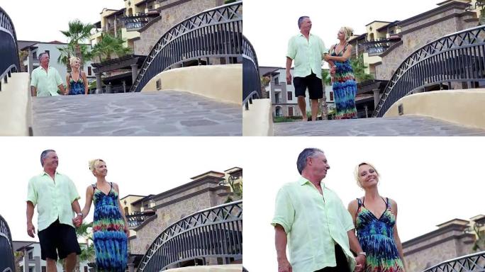一对年长的夫妇牵着手走过度假村的一座小桥