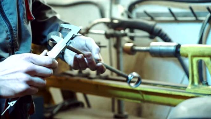 工作形式和手套的机械师在服务室的背景下测量汽车球形接头的高度，宽度和长度。