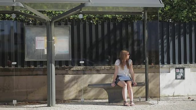 孤独的年轻女孩穿着裙子在公共汽车站等着，夏天