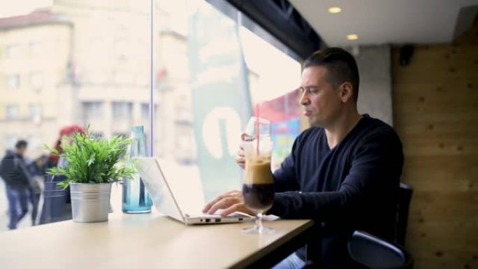 男人在咖啡吧里使用笔记本电脑，喝水