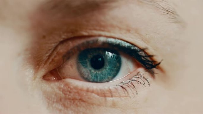 一个涂着睫毛膏的蓝眼睛女人看着相机眨眨眼。单眼特写。