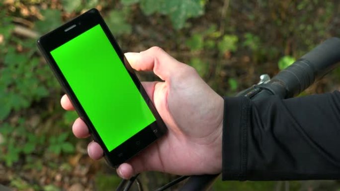 骑自行车的人看着带有绿屏的智能手机-手机上的特写镜头
