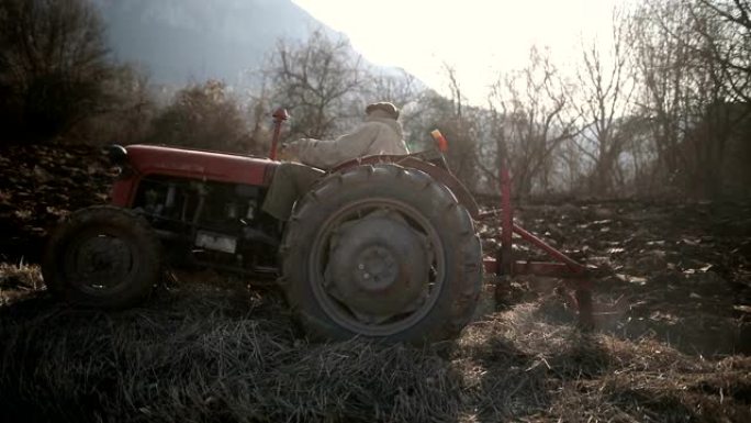 高级男子驾驶小型拖拉机和耕地。农业活动，污染，烟雾