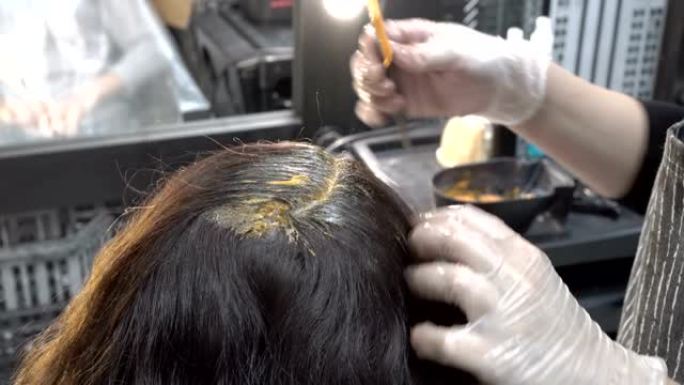 美发师-发型师在美容院为女孩的头发涂漆，并使其涂成棕色。头发护理。特写。从顶部后部看到的景色。4K。