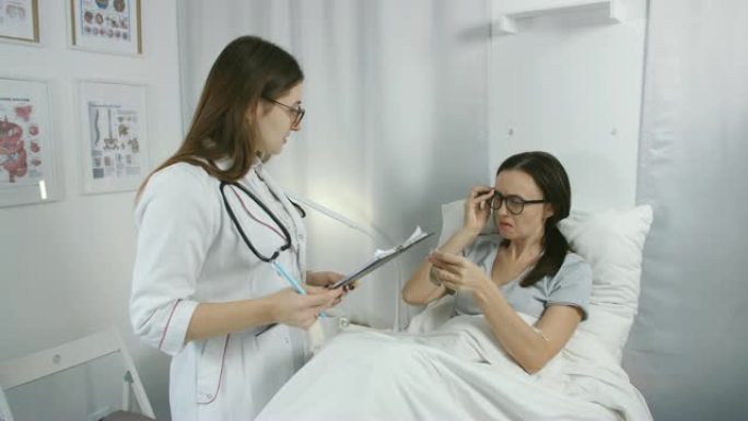在医院里，友好的女医生检查躺在床上的患病女患者，他报告了他的投诉。他们友好地聊天，希望早日康复。