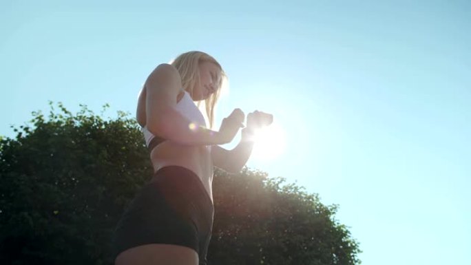 穿着运动胸罩和短裤的年轻女子的低角度视角站在户外阳光下，晨跑训练后在她的健身跟踪器上浏览结果