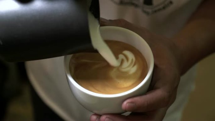在酒吧关闭咖啡师手工制作咖啡艺术。如何用热牛奶制作咖啡艺术，将蒸牛奶倒入咖啡中进行咖啡艺术。工业食品