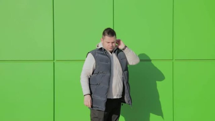 一个胖子靠着商店附近的绿色墙摆姿势