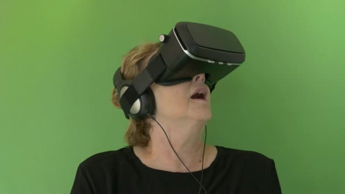 戴着耳机和VR谷歌的高级女性在绿屏中取出