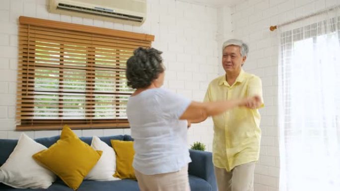 亚洲老年夫妇喜欢在家客厅跳舞。在家老化的概念。
