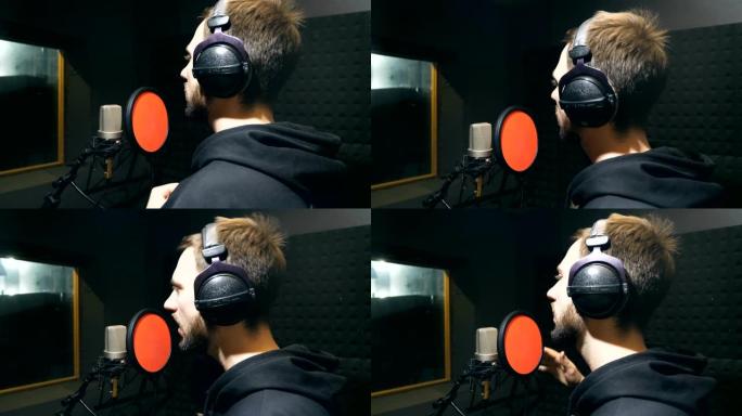 耳机里留着胡子的男歌手在录音棚的麦克风里唱歌。年轻人录制新的旋律或歌曲。创意音乐家的工作。展示商业概