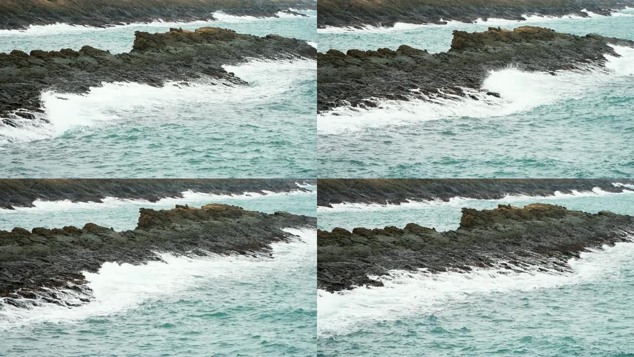 4k缓慢放大拍摄海浪撞击多岩石的海岸。海浪溅到石头上，溪流猛烈流过许多岩石。