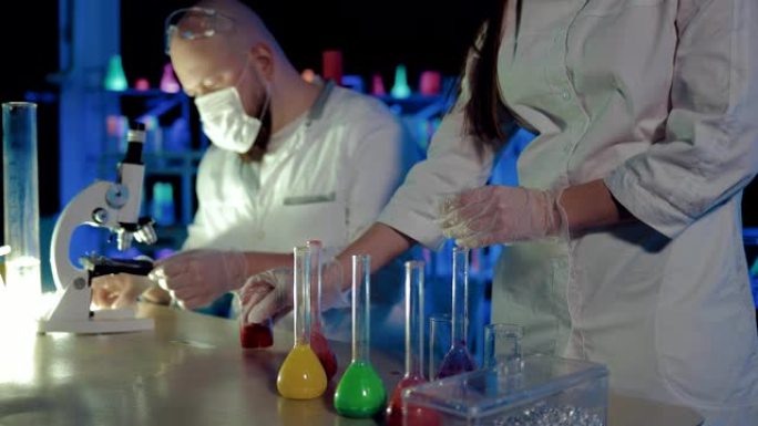 液体从烧瓶中倒入透明烧杯中。化学实验。科学家化学家通过显微镜观察。