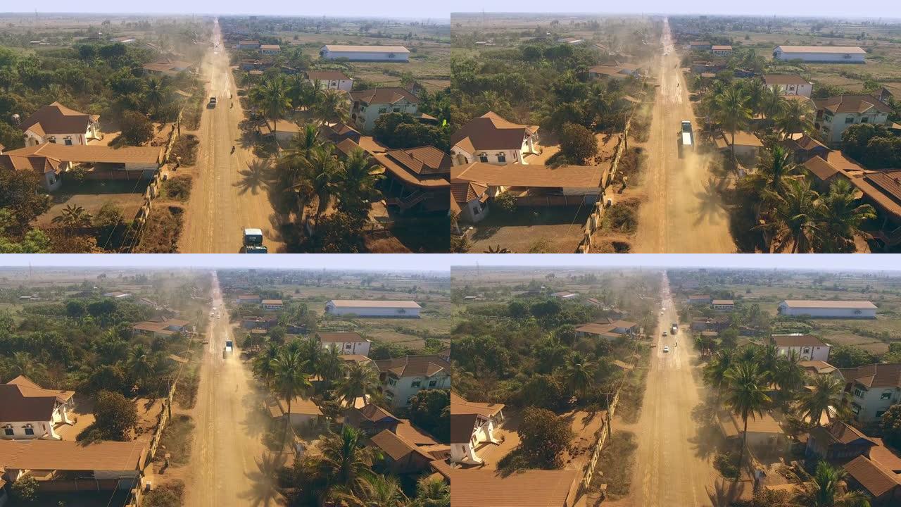 空中无人机射击: 在尘土飞扬的道路上飞越穿越小村庄的车辆