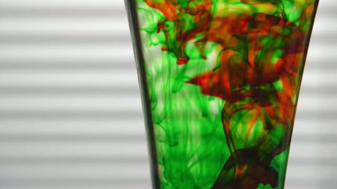 绿色和红色染料溶解在白色背景上的玻璃水中