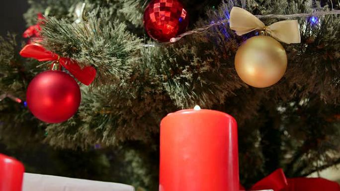 在装饰有红色和金色球的圣诞树下燃烧蜡烛