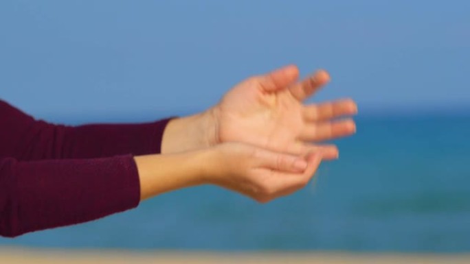 一个年轻的女人在阳光明媚的日子里从一只手向另一只手倾泻金沙。生命的象征 -- 自由流动的沙子