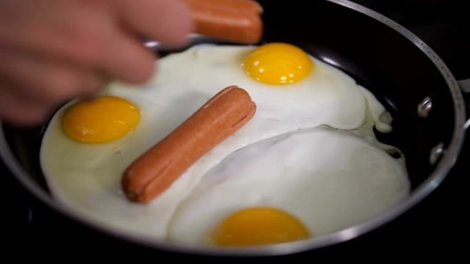 特写。早餐炒鸡蛋。雌性的手向鸡蛋扔香肠。4k慢速移动