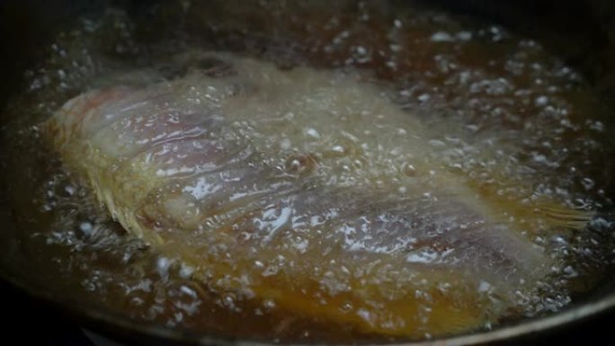 厨师用锅铲舀沸腾的棕榈油，将鱼倒入锅中，直到金黄色。自制油炸鱼。4k镜头。