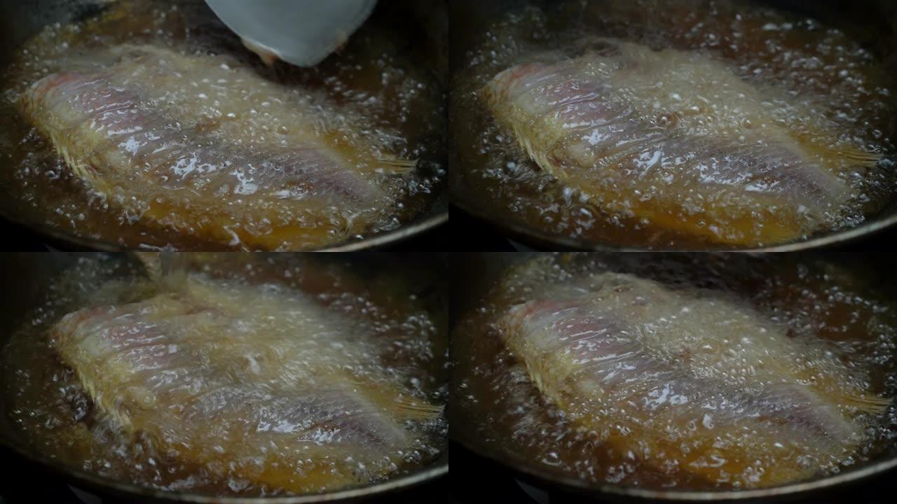厨师用锅铲舀沸腾的棕榈油，将鱼倒入锅中，直到金黄色。自制油炸鱼。4k镜头。