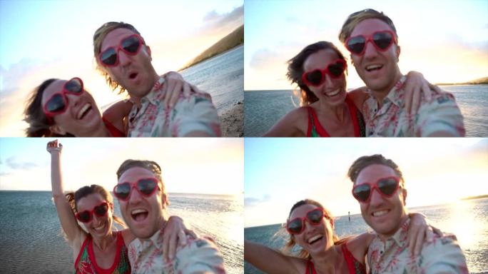 自拍: 海滩上的年轻夫妇在日落时玩得开心，用心形太阳镜自拍。慢动作