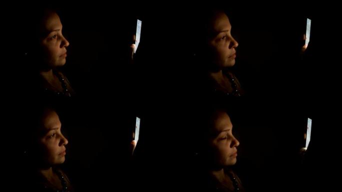 一名中年白人妇女晚上坐在沙发上的房间里，拿着智能手机，与社交网络上的朋友交流