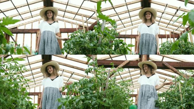 戴着草帽和连衣裙的微笑女农夫带着喷壶去温室