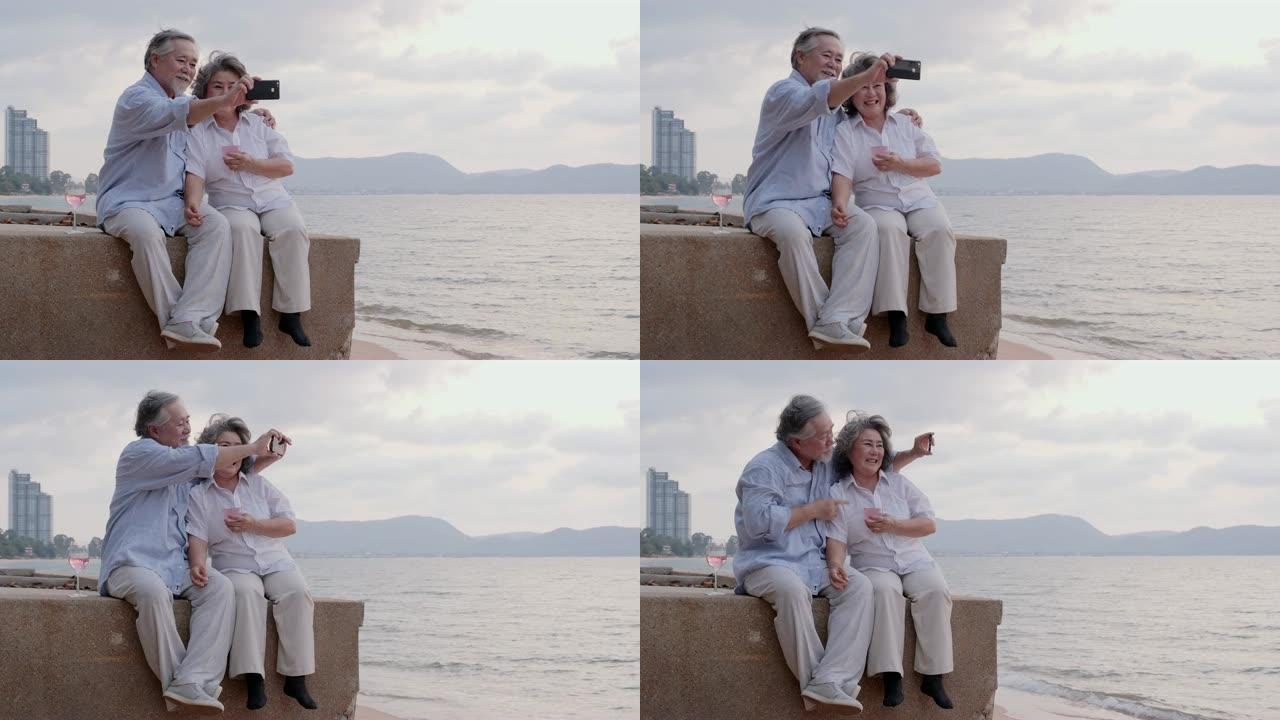 亚洲资深夫妇一起用智能手机在海滩上自拍，情绪愉快。有生活方式、退休和科技观念的人。