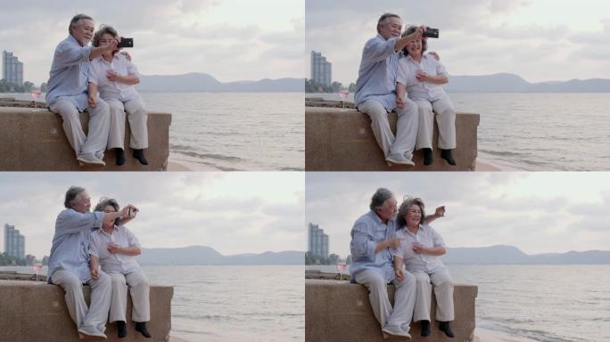 亚洲资深夫妇一起用智能手机在海滩上自拍，情绪愉快。有生活方式、退休和科技观念的人。