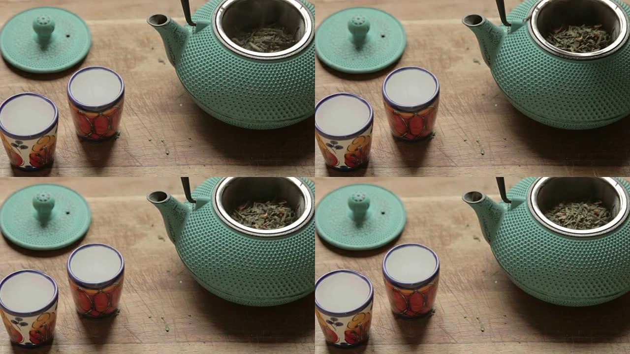 人手将新鲜的药草放入带有两个彩色陶瓷杯的茶箱中