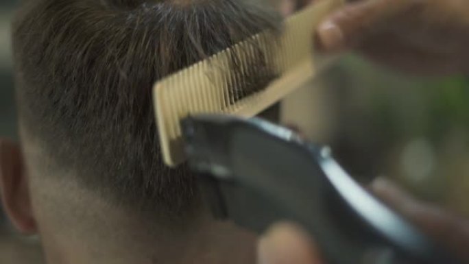理发师在理发店用发发器和梳子理发。理发师在男性沙龙用电动剃须刀做发型。用修剪器和发刷关闭美发