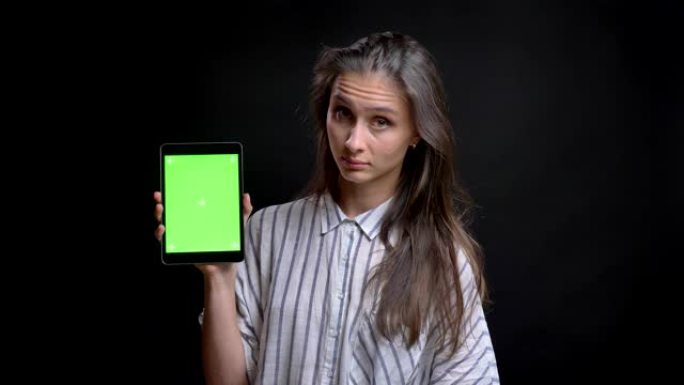 美丽的白人长头发女人的肖像显示绿色屏幕的平板电脑对黑色背景的相机。