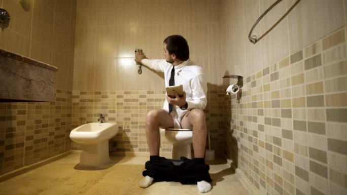 一个男人坐在豪华洗手间的马桶上，拿着电话工作。全高清