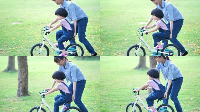 有母亲的亚洲家庭教她的女儿或孩子女孩骑自行车在大自然或公园和阳光中玩耍。慢动作