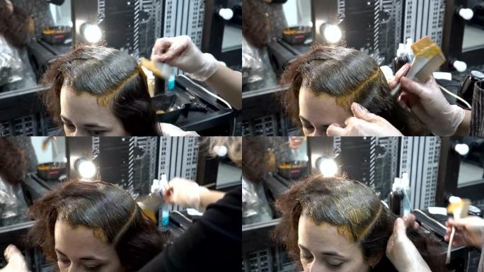 理发店里的东方女孩染发剂。理发师-造型师在她的头上涂上油漆。头发护理。特写。4 k.25 fps。