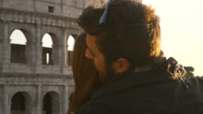 浪漫的年轻夫妇游客日落时在罗马斗兽场前做著名的泰坦尼克号场景男友抱着女朋友张开双臂