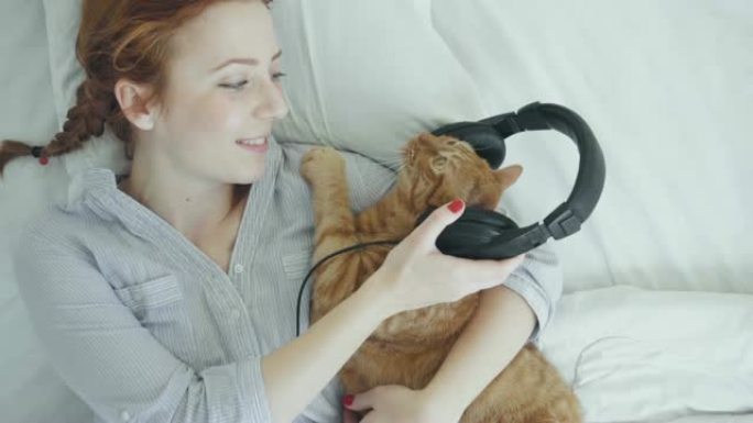 大红猫戴着耳机听音乐，和年轻女子躺在床上
