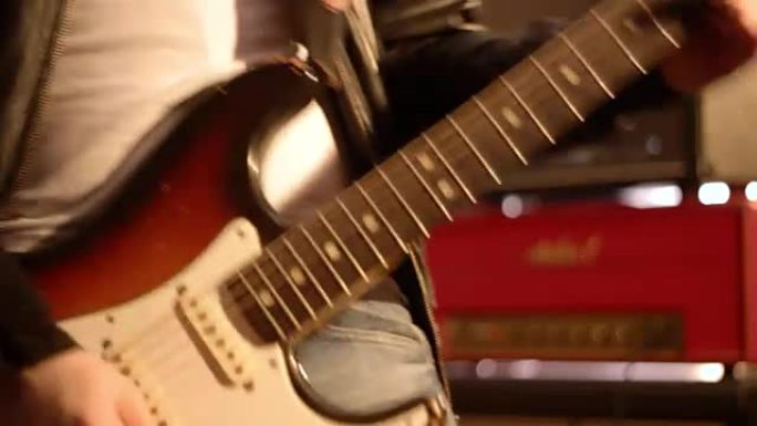 吉他手。一只男性手开始弹电吉他的特写镜头。背景中模糊的放大器和扬声器盒。