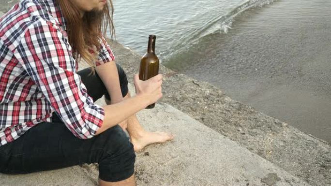 男子沮丧，酒瓶坐在户外4K的海滩上